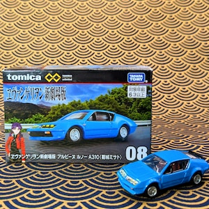 Op de afbeelding: Een blauwe modelauto, naast de doos, met de tekst "Evangelion: 3.0+1.0 Thrice Upon a Time". De doos toont een blauwe auto met een berglandschap. De modelauto is ongeveer 10 cm lang.