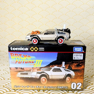 May include: A silver and black Tomica diecast model of the DeLorean time machine from Back to the Future III, with red-rimmed wheels, sitting atop its original box. The box features the movie title and a picture of the car. The text on the box reads "Back to the Future III".