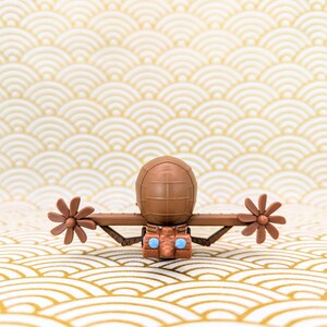 May include: A brown toy submarine with two propellers and blue eyes. The submarine is sitting on a white and gold patterned surface.