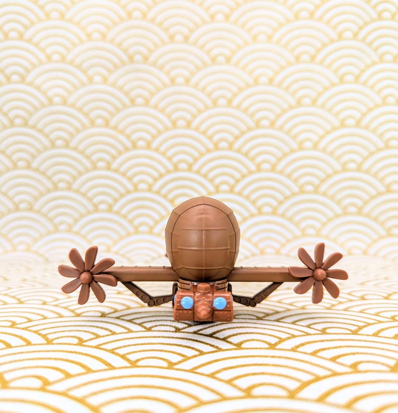 May include: A brown toy submarine with two propellers and blue eyes. The submarine is sitting on a white and gold patterned surface.