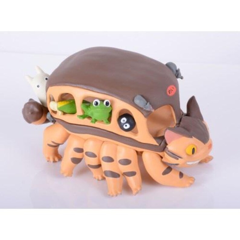 May include: A whimsical, orange and brown figurine resembling a cat-like creature with multiple legs. The figurine has a brown shell-like top and features small figures of a frog, a white creature, and a black soot sprite. The Japanese text is visible on the side.