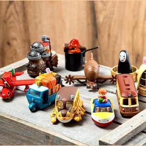 Peut inclure: Une collection de v&eacute;hicules et de figurines jouets color&eacute;s, dont un avion rouge, un camion bleu et orange et un bus jaune. D'autres figurines incluent un train, un personnage en noir et une figurine avec un n&oelig;ud rose.