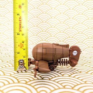 May include: A brown toy airplane with a skull and crossbones design on the tail. The airplane is about 3 inches long and is sitting on a patterned surface.