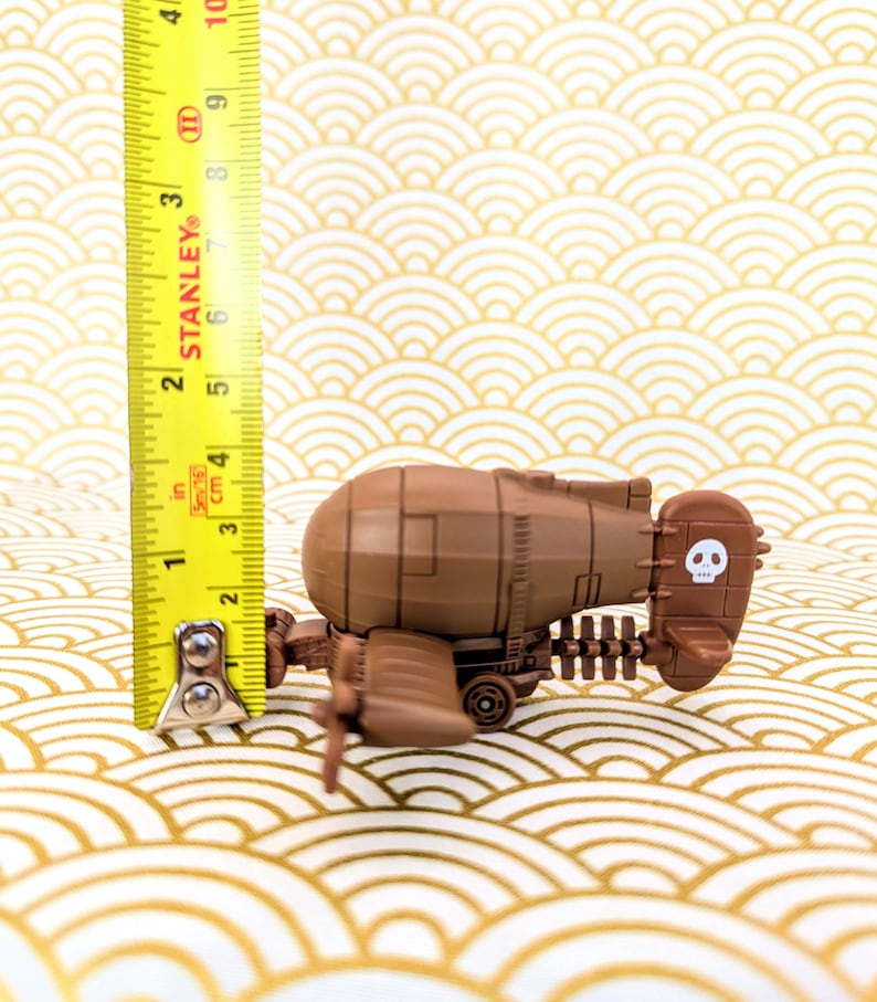 May include: A brown toy airplane with a skull and crossbones design on the tail. The airplane is about 3 inches long and is sitting on a patterned surface.