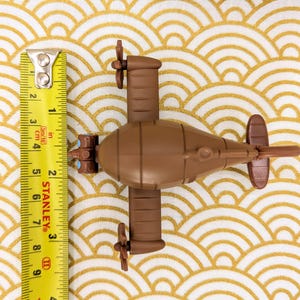 May include: A brown toy submarine with two propellers on each side. The submarine is about 6 inches long and has a yellow measuring tape next to it.