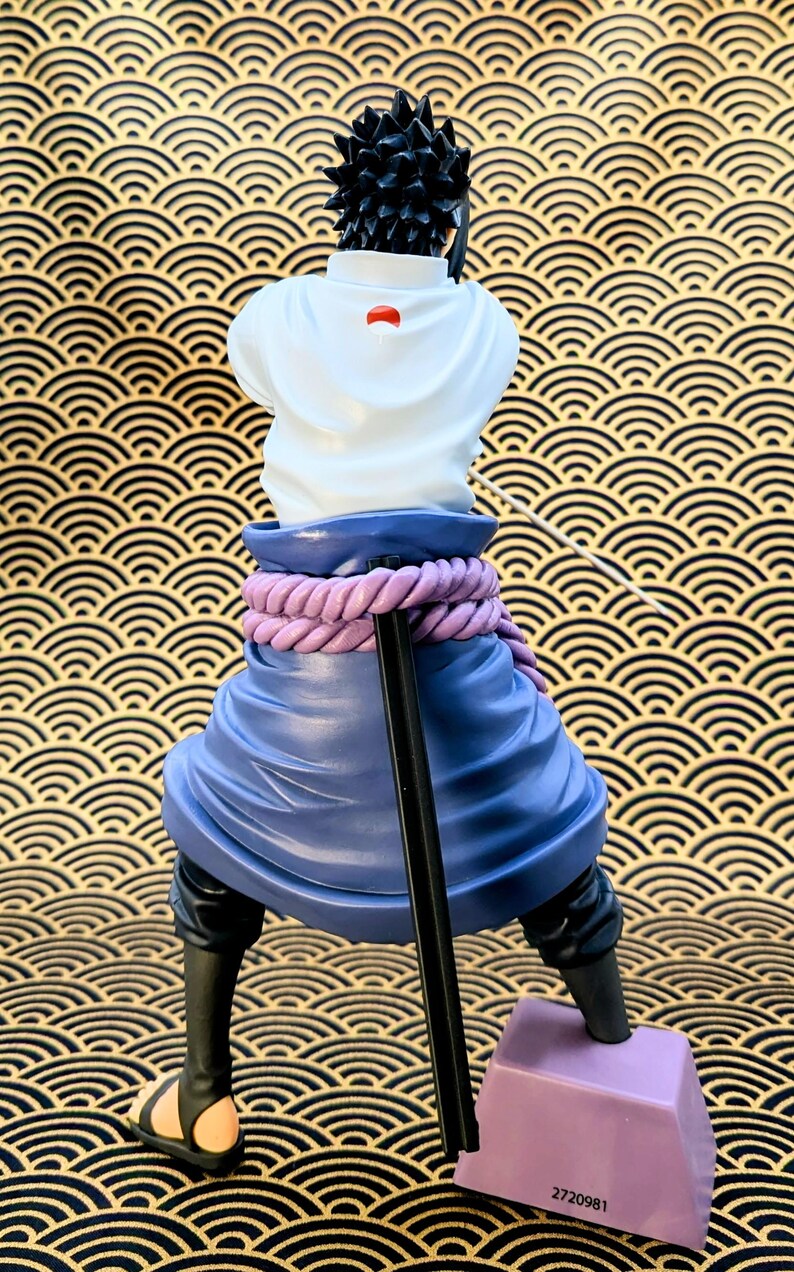 Pode incluir: Estatueta de um personagem com cabelo preto espetado, vestindo uma blusa branca com um emblema vermelho, uma saia azul e sand&aacute;lias pretas. A figura posa com uma bengala, e a base &eacute; roxa. O fundo tem um padr&atilde;o de ondas douradas e pretas.