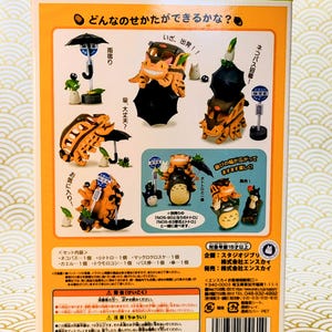 May include: A colorful box featuring various figurines from the animated film "My Neighbor Totoro." The figurines include Totoro characters, a bus, and umbrellas. The box has Japanese text and is designed for ages 15 and up.