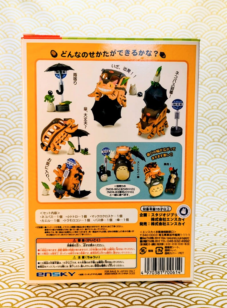 May include: A colorful box featuring various figurines from the animated film "My Neighbor Totoro." The figurines include Totoro characters, a bus, and umbrellas. The box has Japanese text and is designed for ages 15 and up.