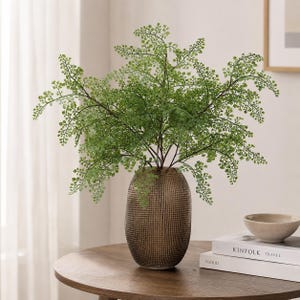 May include: A tall, oval-shaped vase with a dark brown, textured, grid-like surface pattern. The vase holds a large, lush arrangement of vibrant green maidenhair fern stems with delicate, small, fan-shaped leaves and thin, dark brown stems.