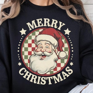 May include: A navy blue sweatshirt featuring a vintage-style Santa Claus graphic within a circular design. The graphic includes the text "MERRY CHRISTMAS" and stars. The Santa illustration has a red hat and a white beard.