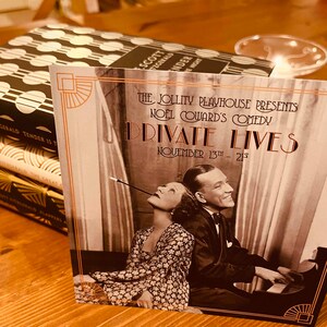 May include: A vintage-style poster advertising a play called "Private Lives" by Noel Coward. The poster features a black and white photo of two actors, a man and a woman, sitting at a piano. The text on the poster is in a gold font and reads "The Jollity Playhouse Presents Noel Coward's Comedy Private Lives November 13th - 21st."