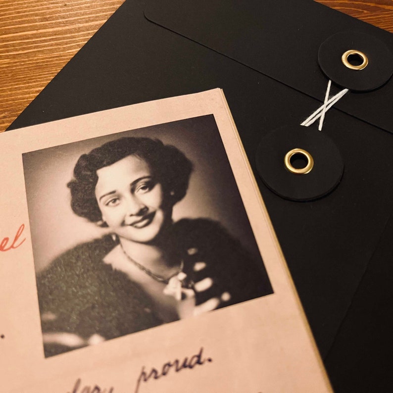 May include: A black and white photo of a woman with dark hair wearing a fur coat. The photo is in a frame and is on a table with a black envelope with two gold and black buttons.