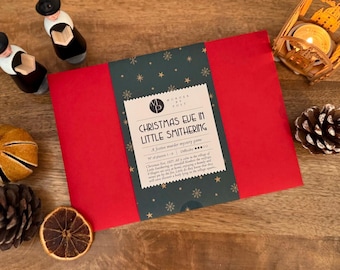 May include: A red box with the title "Christmas Eve in Little Smithering" on a green and gold label. The box is surrounded by decorative items, including wooden figurines, a candle holder, and pine cones, creating a festive holiday theme.