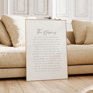 Op de afbeelding: Een wit ingelijst print met een gouden rand met een religieuze quote over zegeningen. De quote luidt "The Blessing" en bevat de tekst "The Lord bless you and keep you, make his face shine upon you and be gracious to you. The Lord turn his face toward you and give you peace. May his favour be upon you and a thousand generations. And your children, and their children, may his presence go before you and behind you and beside you. All around you. You and yours. He is with you. We is with you. In the morning and the evening. In your coming and your going. In your weeping and rejoicing. He is for you. He is for you."
