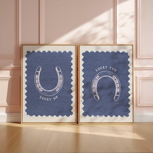May include: Two framed prints with a gold border. Each print features a blue fabric background with a white horseshoe illustration. One print says "Lucky Me" and the other says "Lucky You".