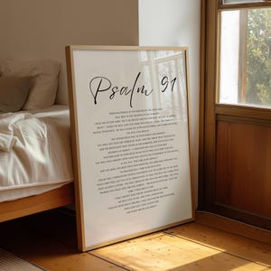 Puede incluir: Una l&aacute;mina enmarcada con el texto Salmo 91 en una fuente negra manuscrita y serif sobre un fondo blanco. La impresi&oacute;n contiene el texto b&iacute;blico completo del Salmo 91. El marco es de madera clara y est&aacute; apoyado verticalmente en el suelo.