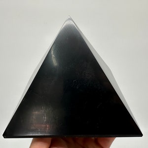 May include: A black obsidian pyramid crystal. The pyramid is smooth and polished, with a reflective surface.