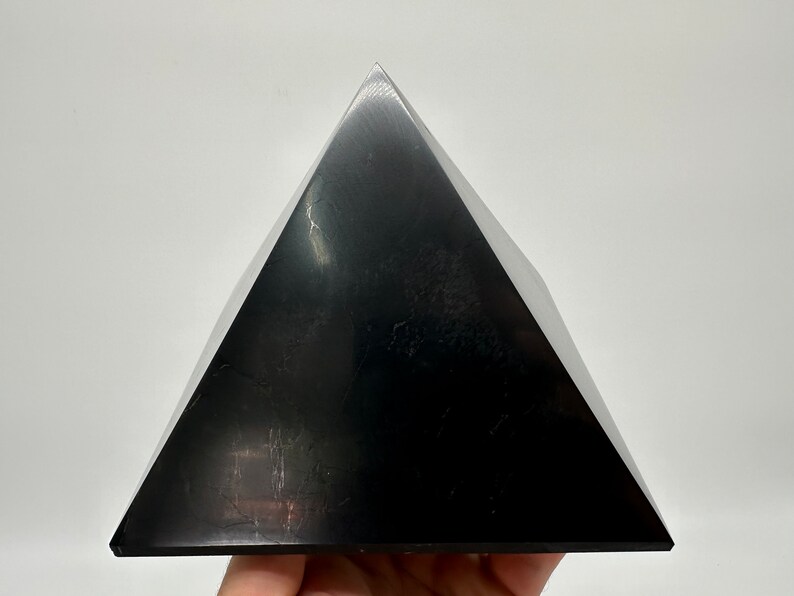 May include: A black obsidian pyramid crystal. The pyramid is smooth and polished, with a reflective surface.