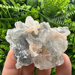 Op de afbeelding: Een cluster van heldere, doorschijnende kristallen met een vleugje roze. De kristallen zijn in een ruwe, natuurlijke formatie geclusterd.