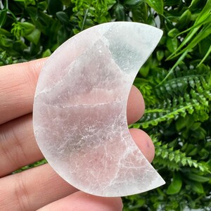 Puede incluir: Un cristal de selenita blanco en forma de media luna. El cristal es liso y pulido con una apariencia translúcida.