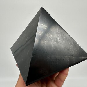 May include: A black obsidian pyramid with a smooth, polished surface. The pyramid has a slightly textured appearance, giving it a unique look.