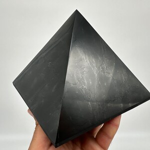 May include: A black obsidian pyramid crystal, a geometric shape with four triangular sides and a square base.