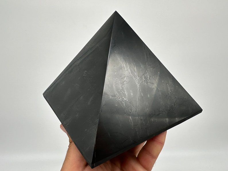 May include: A black obsidian pyramid crystal, a geometric shape with four triangular sides and a square base.