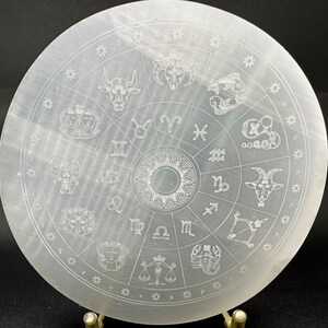 Può includere: Un piatto di ricarica in selenite bianco con un design a ruota zodiacale. Il piatto presenta i dodici segni zodiacali e i loro simboli, tra cui Ariete, Toro, Gemelli, Cancro, Leone, Vergine, Bilancia, Scorpione, Sagittario, Capricorno, Acquario e Pesci.
