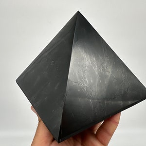 May include: A black obsidian pyramid, a polished, geometric crystal with a smooth, reflective surface.