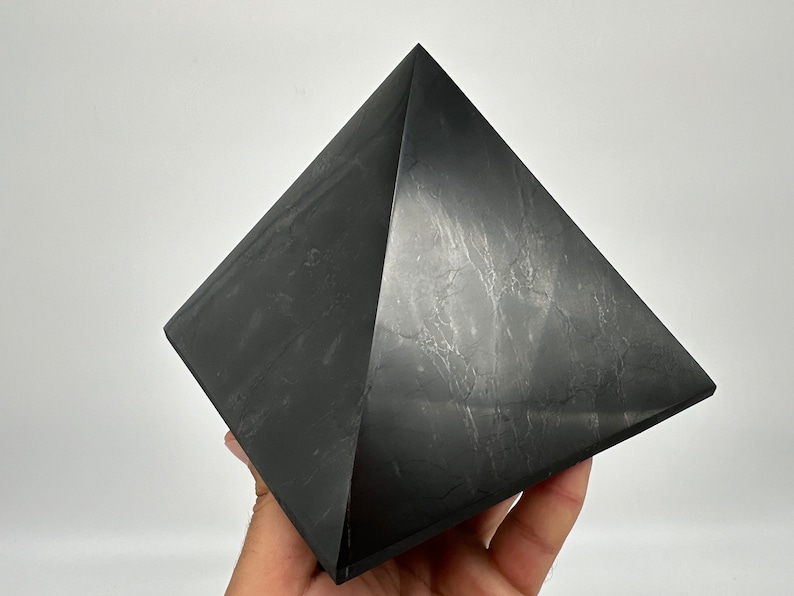 May include: A black obsidian pyramid, a polished, geometric crystal with a smooth, reflective surface.