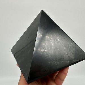 May include: A black obsidian pyramid with a smooth, polished surface. The pyramid has a slightly textured appearance with subtle white veins running through the stone.