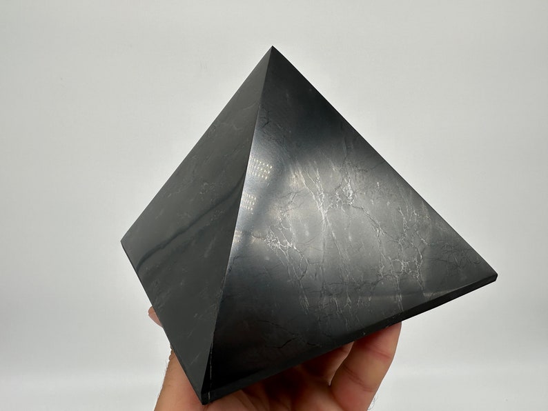 May include: A black obsidian pyramid with a smooth, polished surface. The pyramid has a slightly textured appearance with subtle white veins running through the stone.