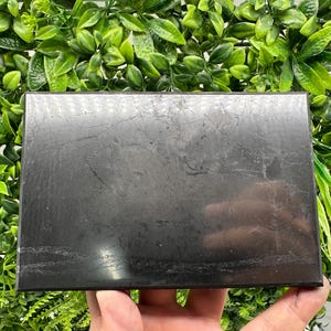 May include: A black rectangular slab of polished stone with a smooth, glossy surface. The stone has a subtle veining pattern.