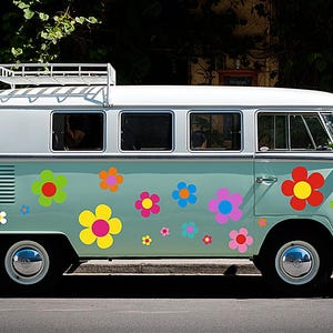 Könnte beinhalten: Ein hellblau-weißer Vintage-Volkswagen-Bus, verziert mit bunten Blumenaufklebern. Der Bus hat einen weißen Dachgepäckträger und Chromradkappen. Das Fahrzeug parkt auf einer Straße.