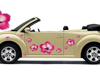 May include: A beige convertible car adorned with pink and white hibiscus flower decals. The car has black tyres and a black convertible top. The car is a classic style.