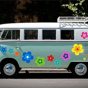 Könnte beinhalten: Ein türkisfarbener und weißer VW-Bus im Vintage-Stil, verziert mit bunten Blumenaufklebern. Der Bus hat einen weißen Dachträger und Chromradkappen. Die Seite des Busses ist mit Blumendesigns in Blau, Rosa, Gelb und Orange verziert.