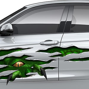Könnte beinhalten: Silberne Autotür mit einem Design eines grünen Monsterauges und Krallen. Das Design erweckt den Eindruck, als würde es durch die Oberfläche des Autos reißen und ein grünes, strukturiertes Innere freilegen. Das Auge ist gelb und die Krallen sind schwarz.