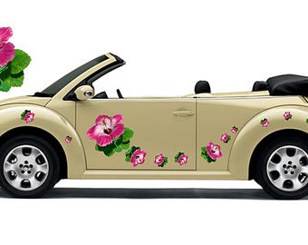 May include: A beige convertible car adorned with pink hibiscus flower decals. The car features black tyres and a black convertible top. The flowers are clustered on the side and rear of the car.