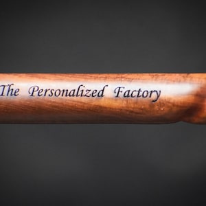 以下が含まれることがあります： 真鍮製の先端が付いた木製の杖のクローズアップ。杖には「The Personalized Factory」という文字が刻まれています。