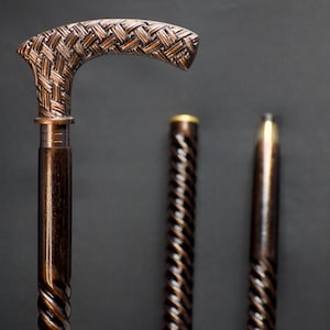 Puede incluir: Un conjunto de tres bastones de paseo con intrincados diseños tejidos. La parte superior de los bastones está hecha de madera marrón oscura con un acabado de color cobre. Los bastones son de diferentes longitudes.