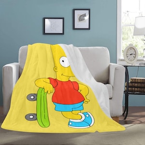 Op de afbeelding: Een gele fleecedeken met Bart Simpson die op een groen skateboard leunt. Bart draagt een rood shirt, een blauwe korte broek en blauwe schoenen. De deken is over een witte bank gedrapeerd.