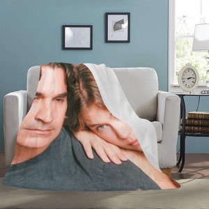 May include: A white blanket draped over a white armchair. The blanket features a printed image of a man and a woman. The man is wearing a gray shirt, and the woman is resting her head on his shoulder.