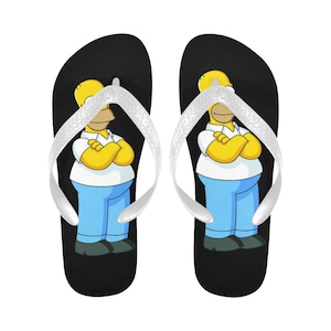 Puede incluir: Un par de chanclas negras con una tira blanca y una imagen de dibujos animados de Homero Simpson en la parte delantera.
