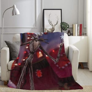 May include: A red, white, and black throw blanket with a graphic of Jack Skellington from the Nightmare Before Christmas movie. The blanket features a red background with a blue sky and stars. Jack Skellington is holding a star in his hand.