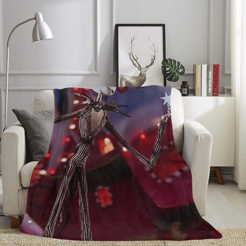 May include: A red, white, and black throw blanket with a graphic of Jack Skellington from the Nightmare Before Christmas movie. The blanket features a red background with a blue sky and stars. Jack Skellington is holding a star in his hand.
