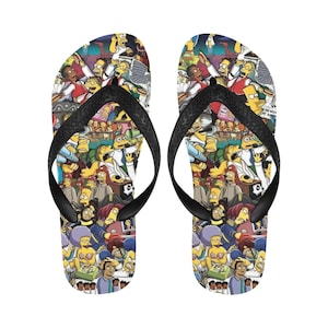 Puede incluir: Un par de chanclas negras con un estampado colorido de varios personajes de Los Simpsons. El estampado incluye personajes amarillos, azules, rojos, verdes y blancos.