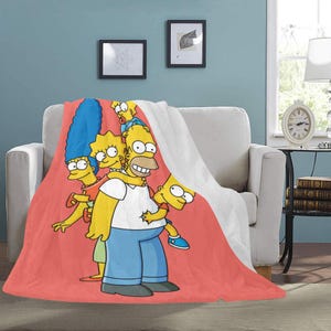 Op de afbeelding: Een rode, witte en gele deken met de Simpsons-familie. Homer, Marge, Bart, Lisa en Maggie zijn afgebeeld in hun iconische gele huid en kenmerkende kleding. De deken is perfect om elke kamer een vleugje plezier te geven.