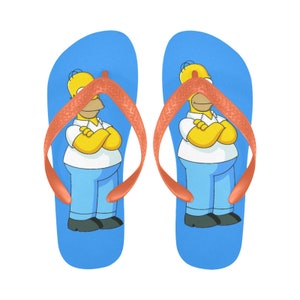Puede incluir: Un par de chanclas azules con una correa naranja y una imagen de dibujos animados de Homero Simpson en cada una.