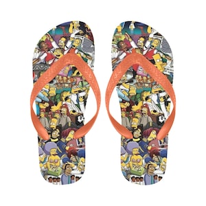 Puede incluir: Un par de chanclas naranjas con un estampado colorido de los personajes de Los Simpson. El estampado incluye a Homer, Marge, Bart, Lisa, Maggie y otros personajes del programa.