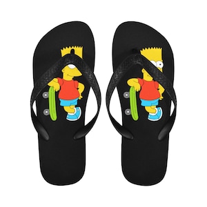 Puede incluir: Un par de chanclas negras con una imagen de dibujos animados de Bart Simpson patinando en cada correa.